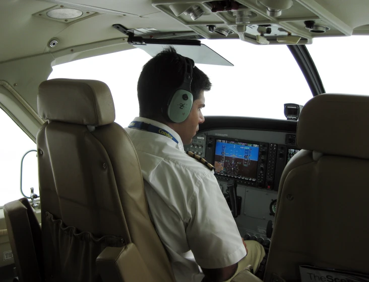 a man in a flight suit in the cockpit of an airplane with two people looking at a computer screen