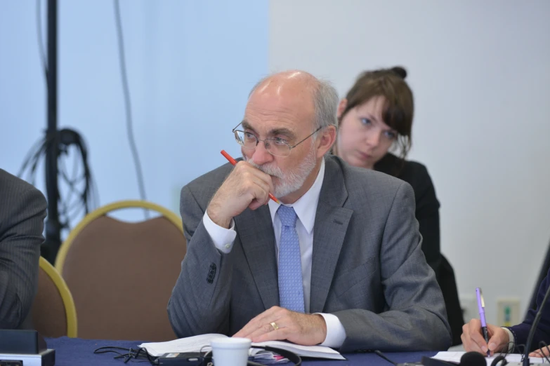 a man in a suit and tie sitting at a table with a paper and pens