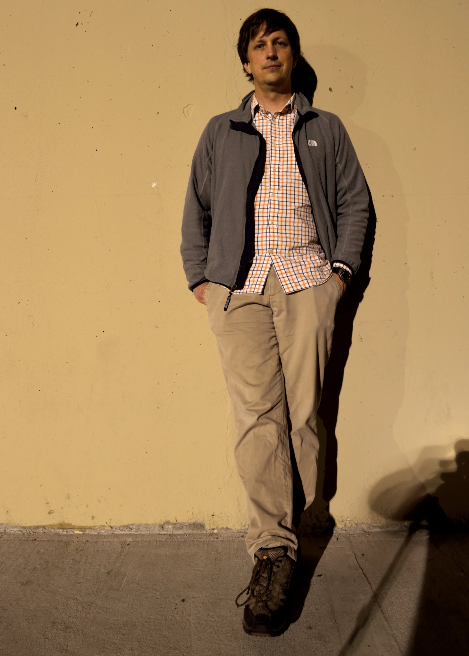 a man standing next to a wall wearing a brown pants