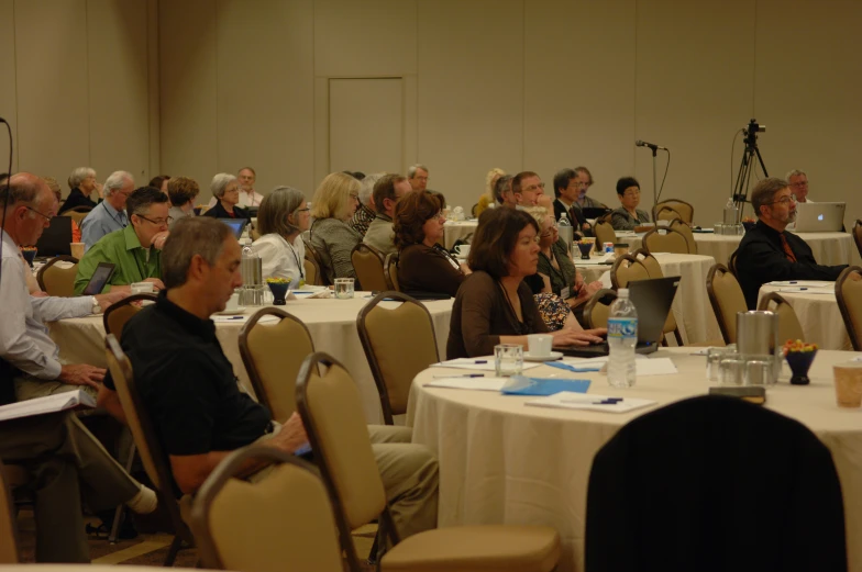 several people sitting at tables with microphones and other people standing around