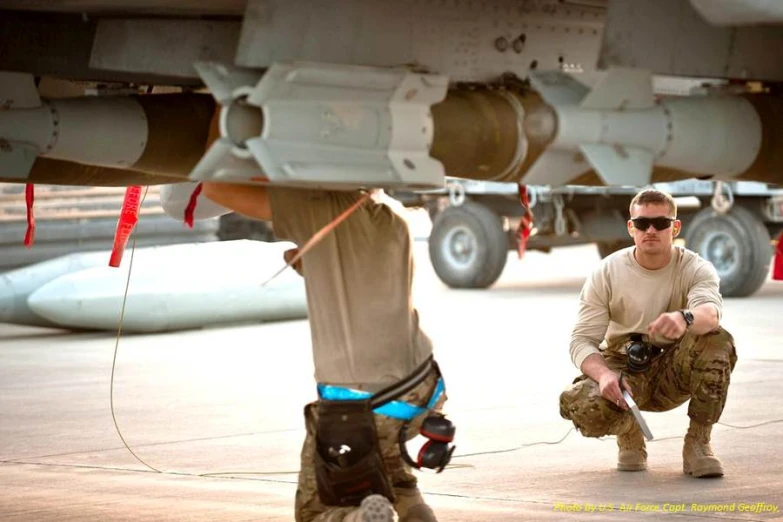 two men crouching with equipment near a jet