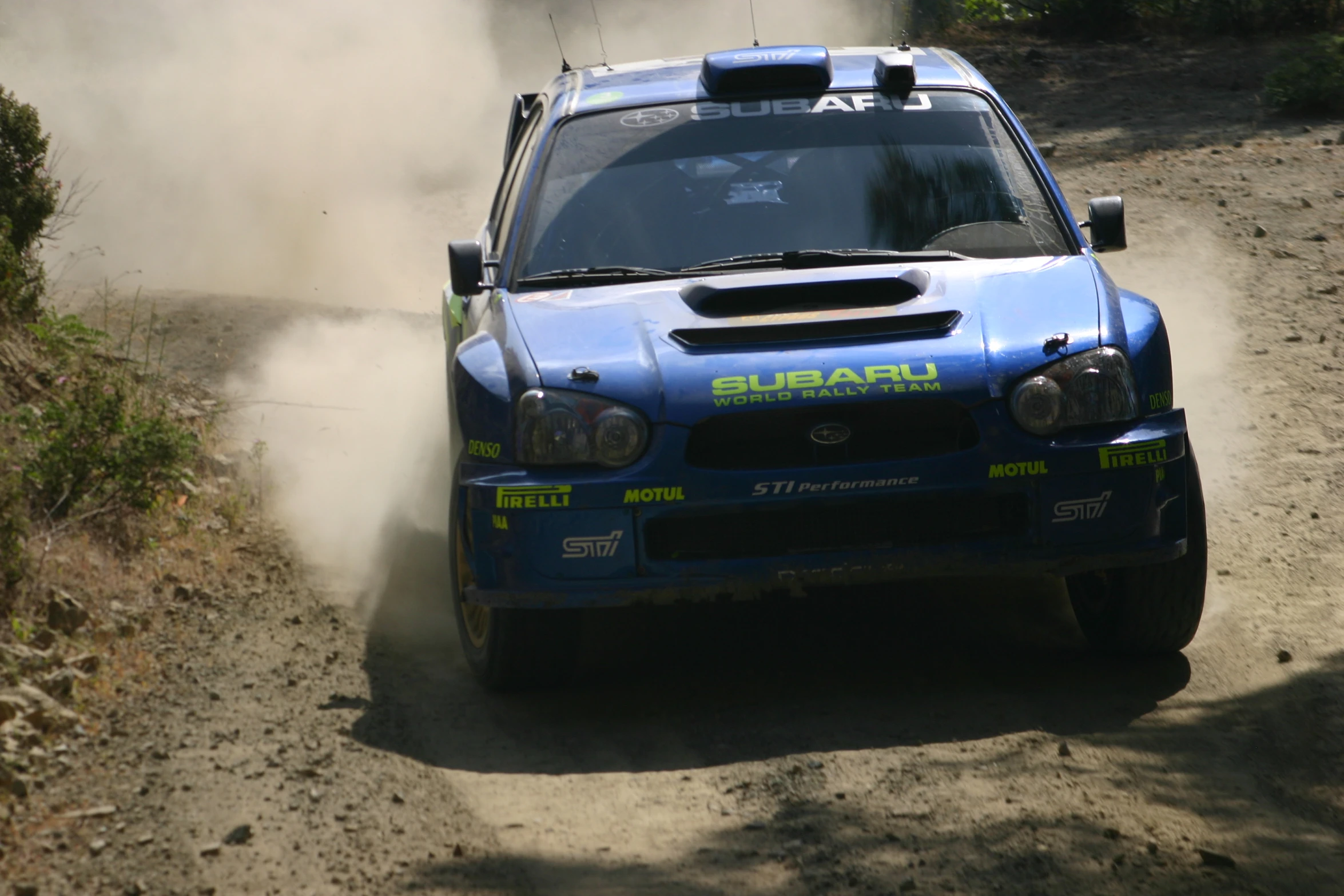 the subaru is a blue rally car in motion on a dirt track