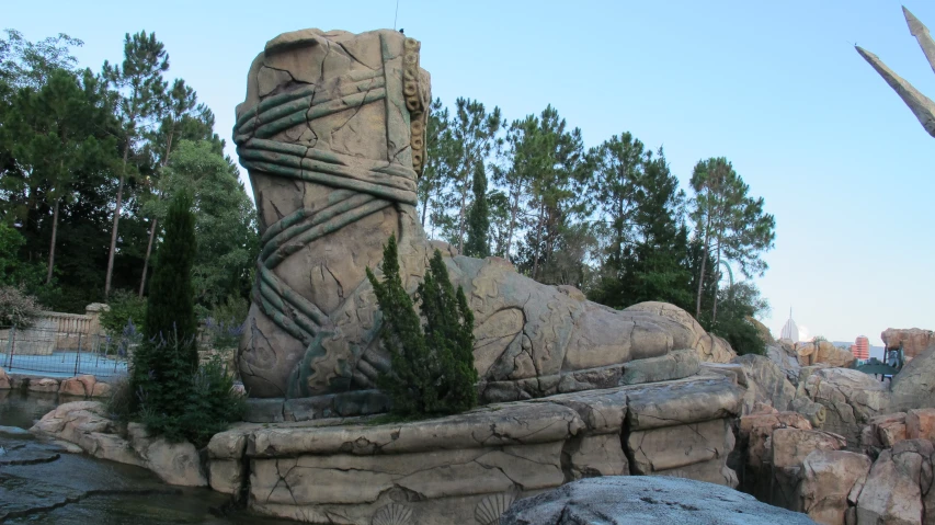 an area features a rock fountain and shrubbery, and tall trees