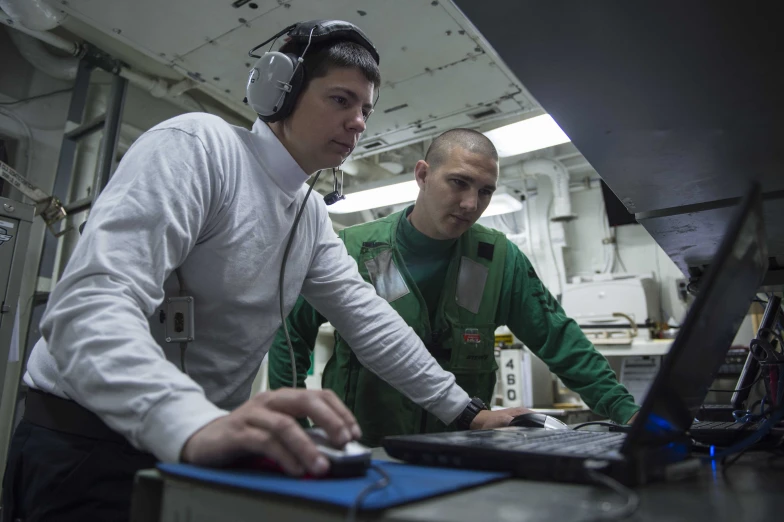 two men with headphones are working on a computer