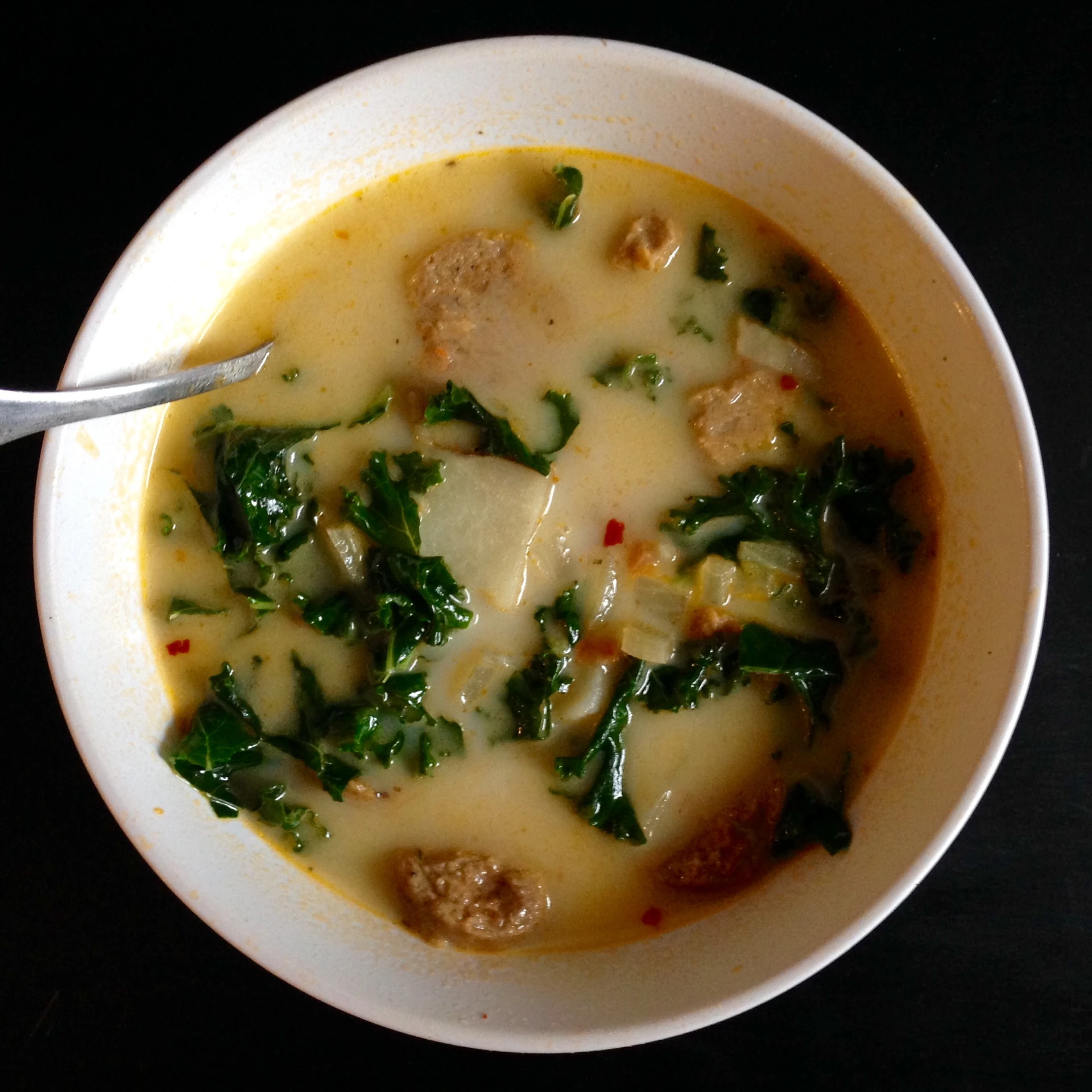 a bowl of soup with spinach and sausages