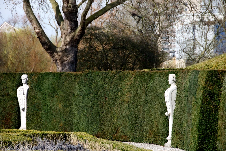 two statues in front of some shrubbery and a tree