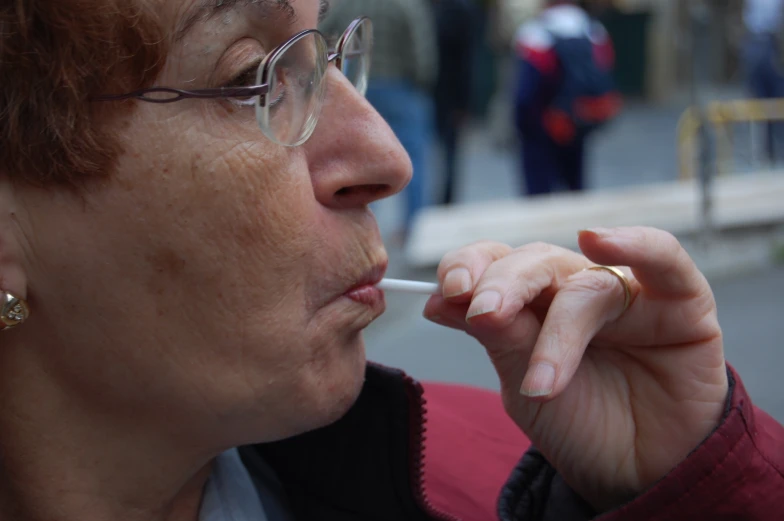 woman with glasses smoking on street corner while wearing jacket