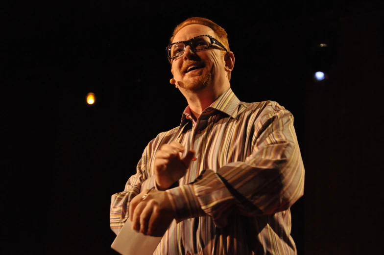 a man with glasses standing on stage in front of microphone