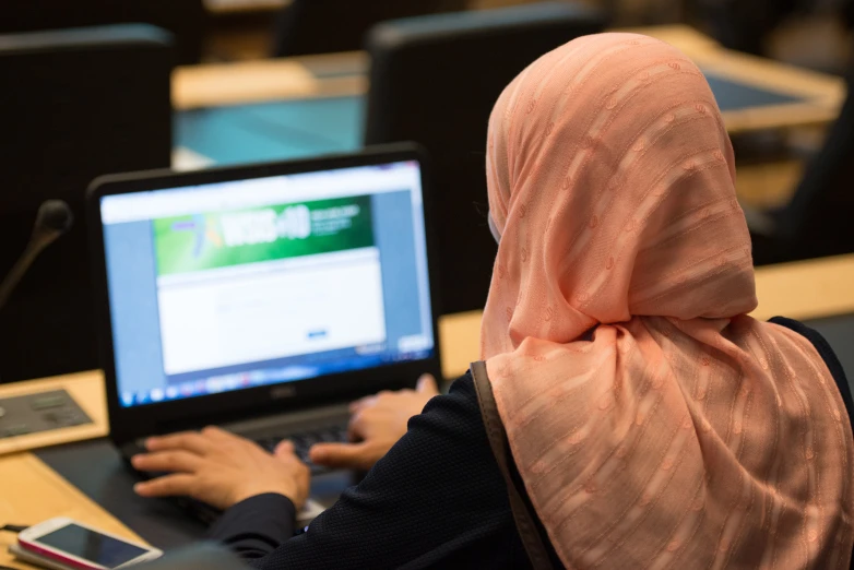 woman in hijab sitting at table with laptop in front of her