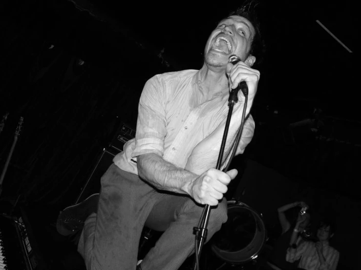 a man is singing into a microphone while standing on a stool