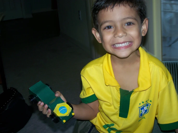a boy smiling and holding a green and yellow soccer uniform