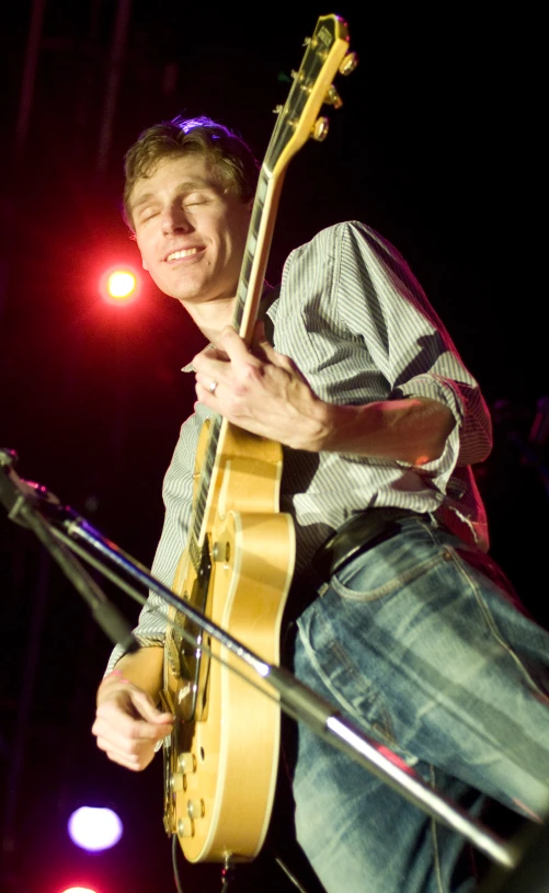 a man holding an acoustic guitar with a mic next to him