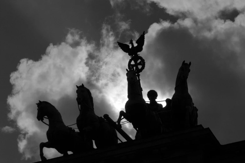 black and white pograph of three statues on a building with clouds