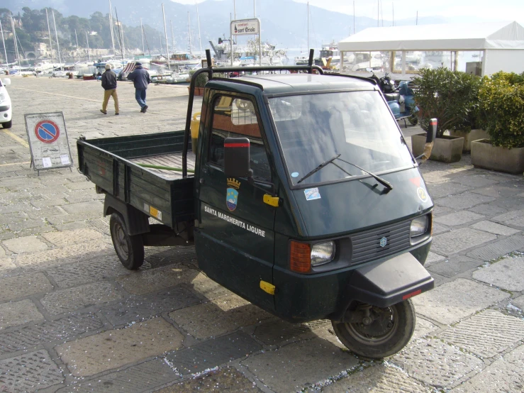 a small green truck parked next to people on a sidewalk