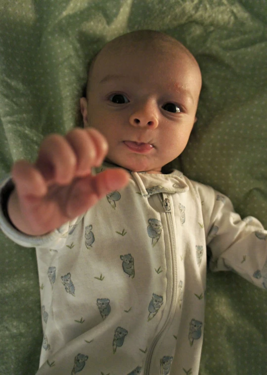 a baby laying on a green sheet touching soing with it's hand