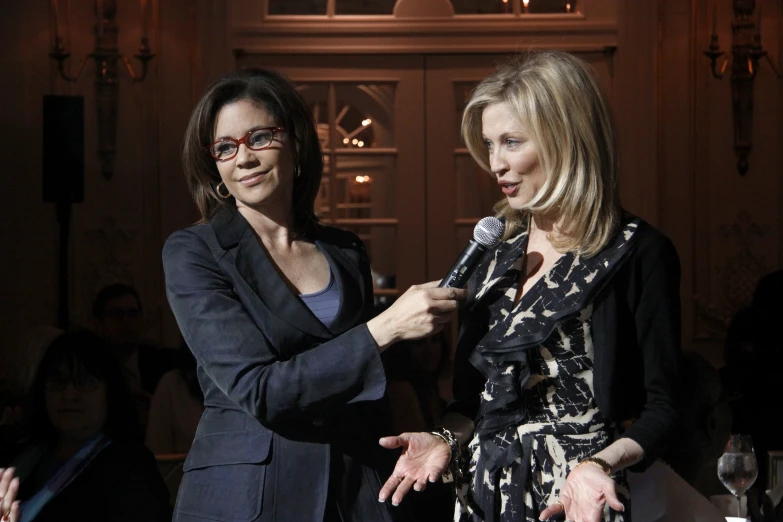 two women standing next to each other talking into a microphone