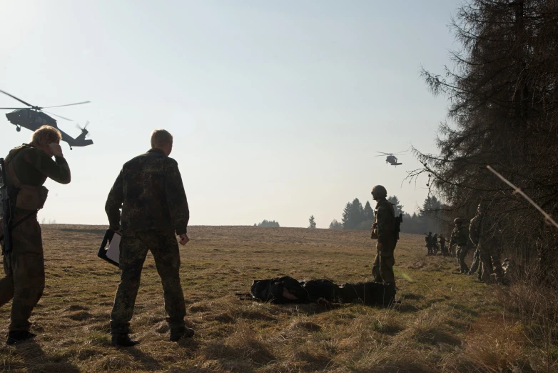 three soldiers are standing in the field with a helicopter