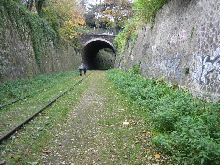 two men walking down the train tracks into an old tunnel