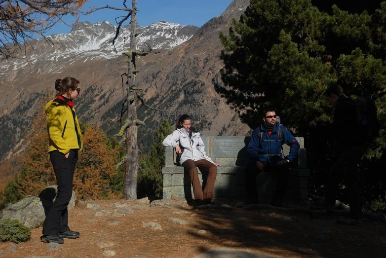 three people wearing jackets standing near the mountains