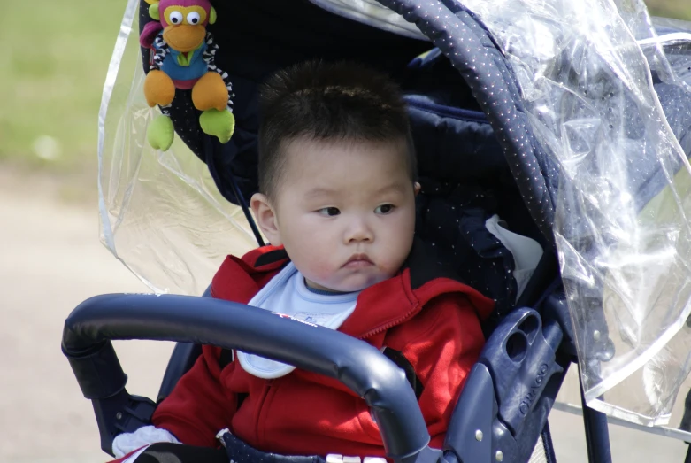 an asian toddler wearing a red coat and holding on to a stroller