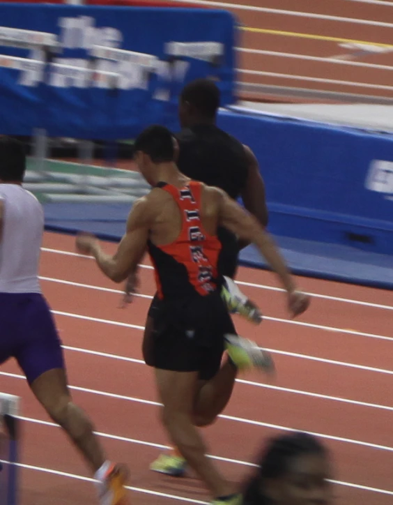 two men running in a race, one is wearing an orange vest