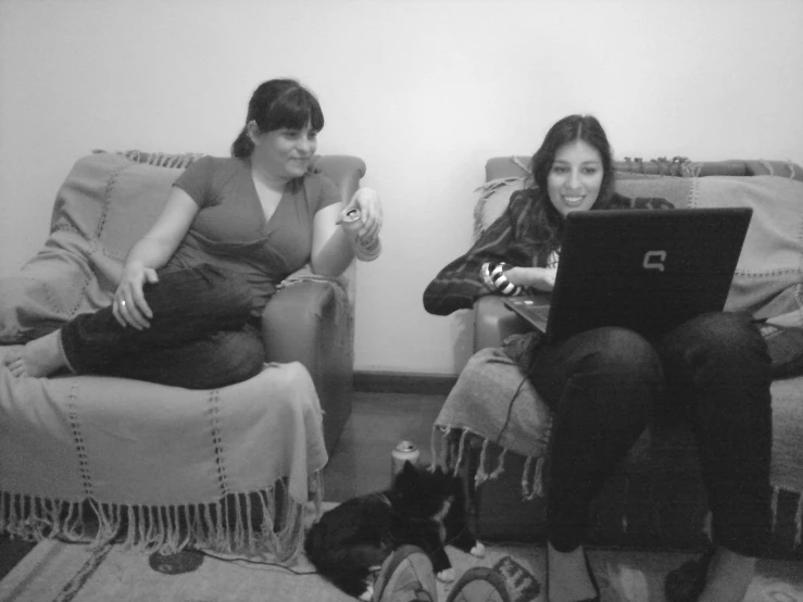 two women sit on the couch playing games on their laptops