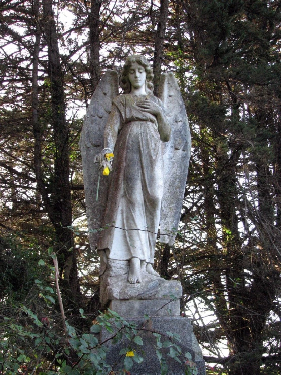 a concrete angel statue in between some trees