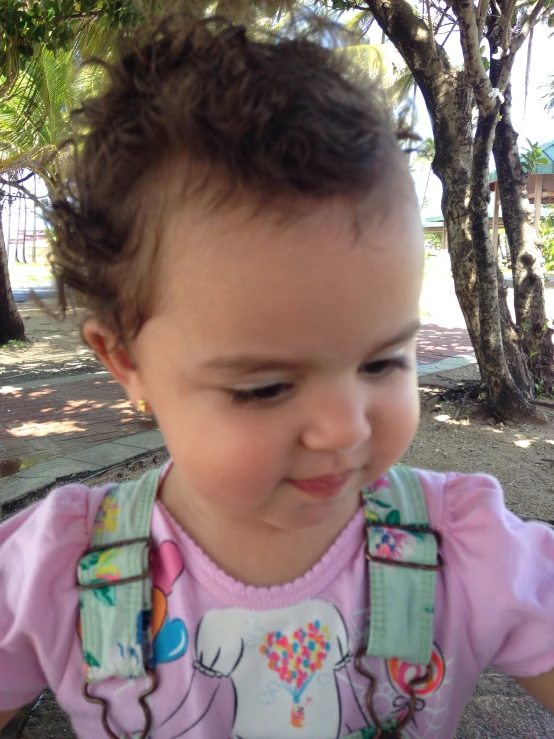 a baby girl standing under a tree wearing an apron