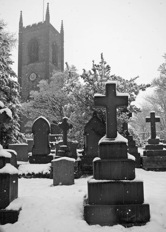 a graveyard with snow and trees with a cathedral in the background