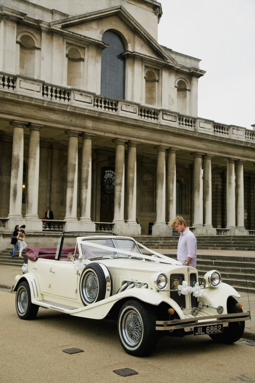 man in white shirt and brown pants leaning on convertible car