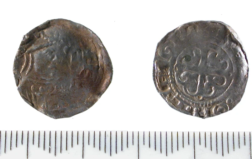 two ancient coins on a ruler that have been given to them