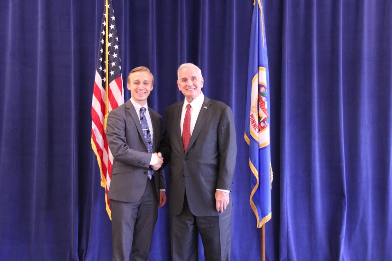 two men in business suits standing in front of flags