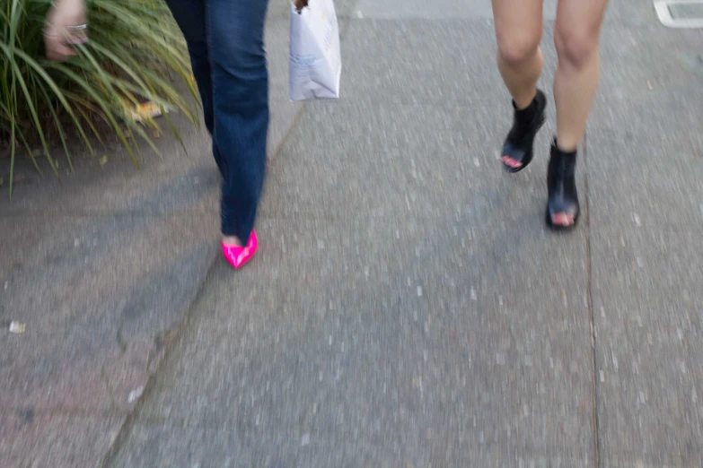 two women walking down a sidewalk with shopping bags