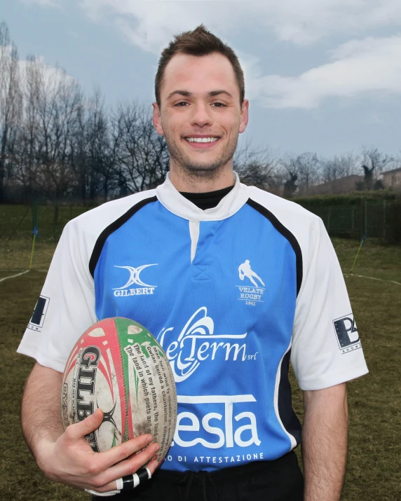 man in blue uniform holding rugby ball in grassy area