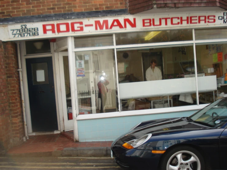 a man walks out the door of a store front with a car parked in front