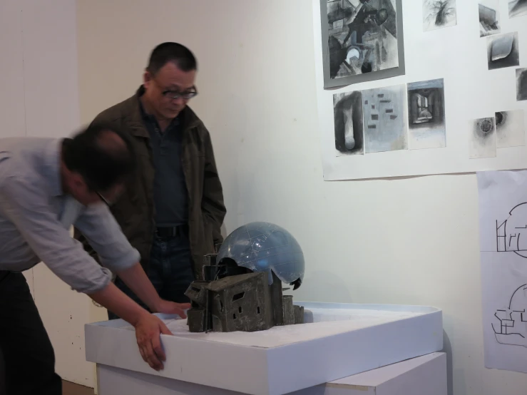 two men looking at a sculpture displayed on top of a table