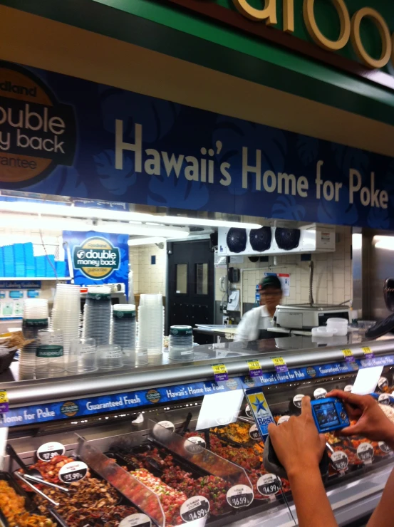 a display case in a food market that has a person in the background working on his digital device