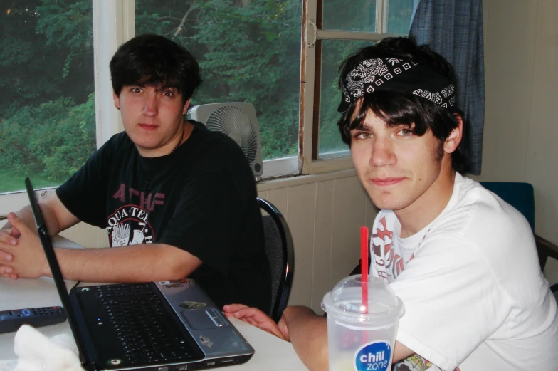 two boys sitting at a table with computers