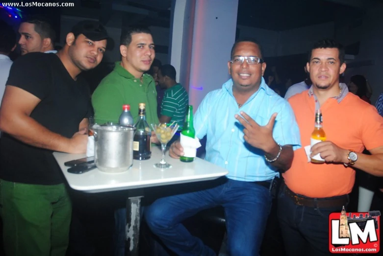 men pose for a po in front of bottles and wine