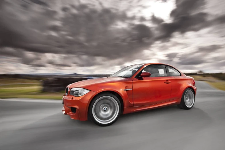 a red car is driving down the road under cloudy skies