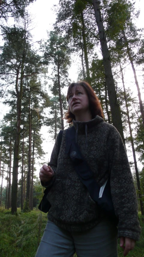 a woman standing in the woods looking up into the trees