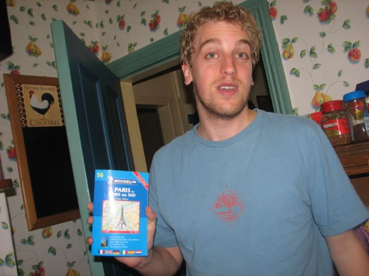 man standing in a room with blue flowered walls holding up his boxed package