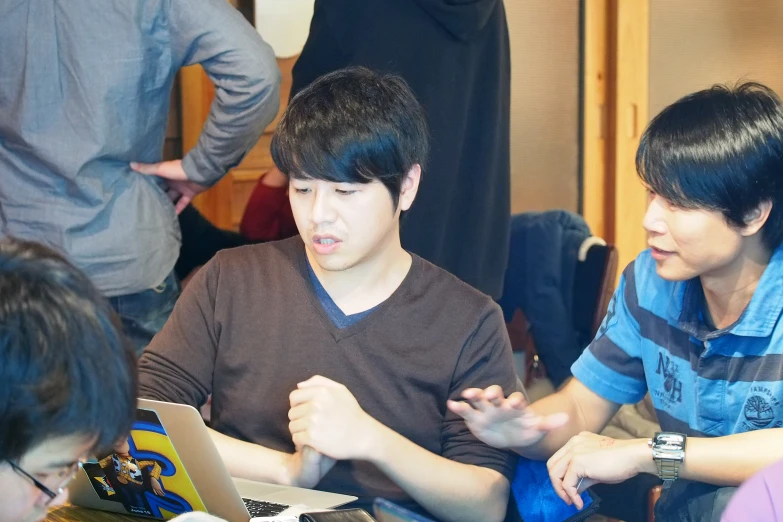 two people working at a table with laptops and other people