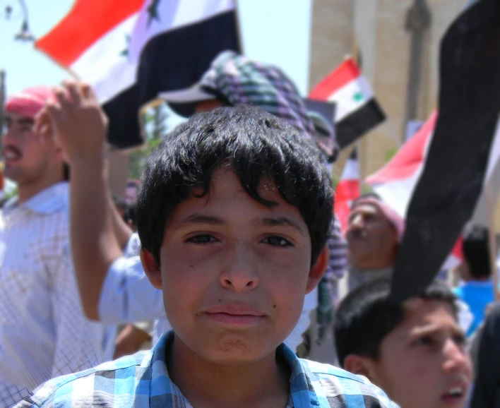 a small boy stands among many other people at an outdoor event