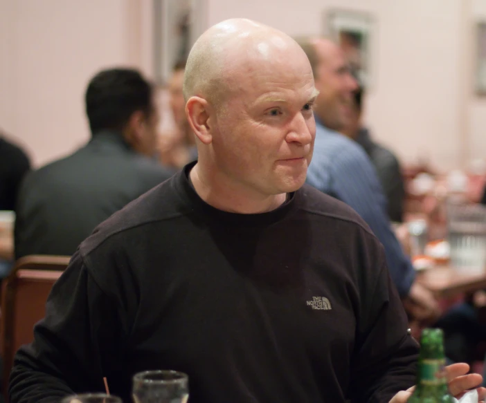 bald headed man sitting at the table with several glasses