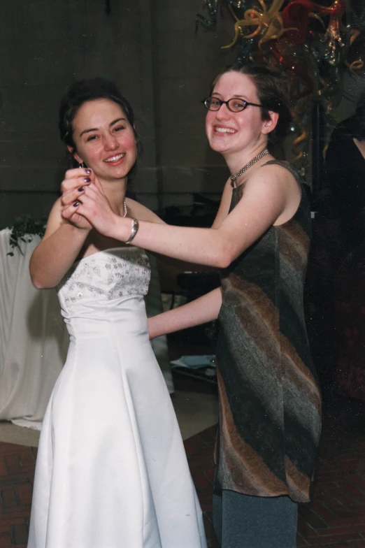 two women dancing together in a white dress