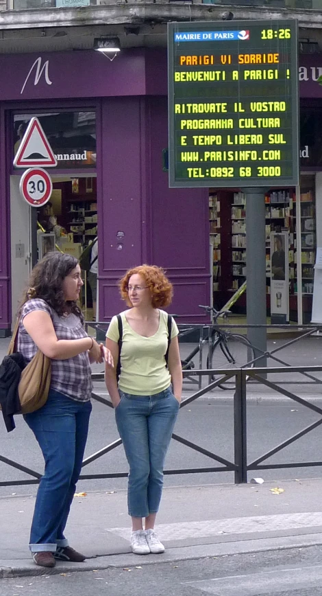 two people standing near a road by a purple building