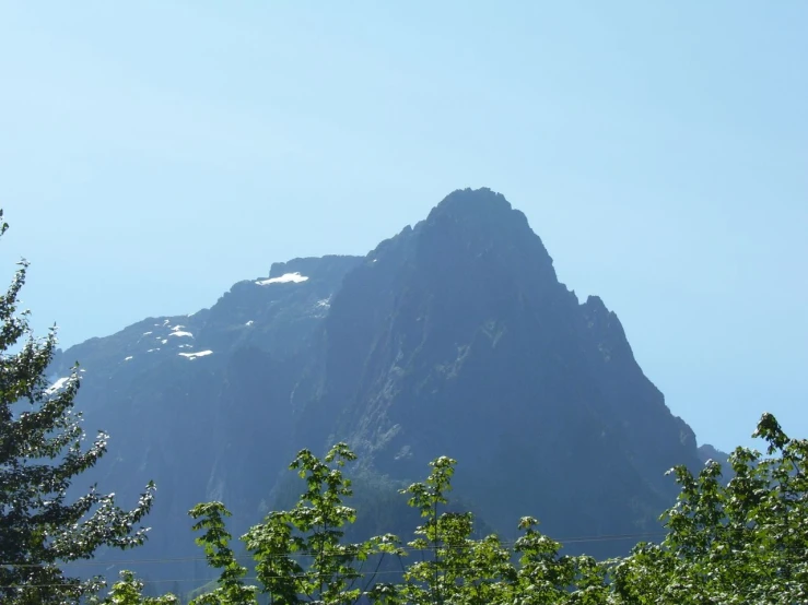 the top of a mountain rising above trees with snow on it