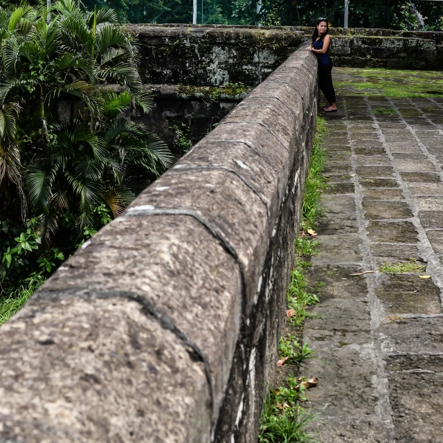 a person sits on a stone path over a stone wall