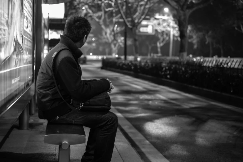 a person sitting on a bench on the sidewalk at night